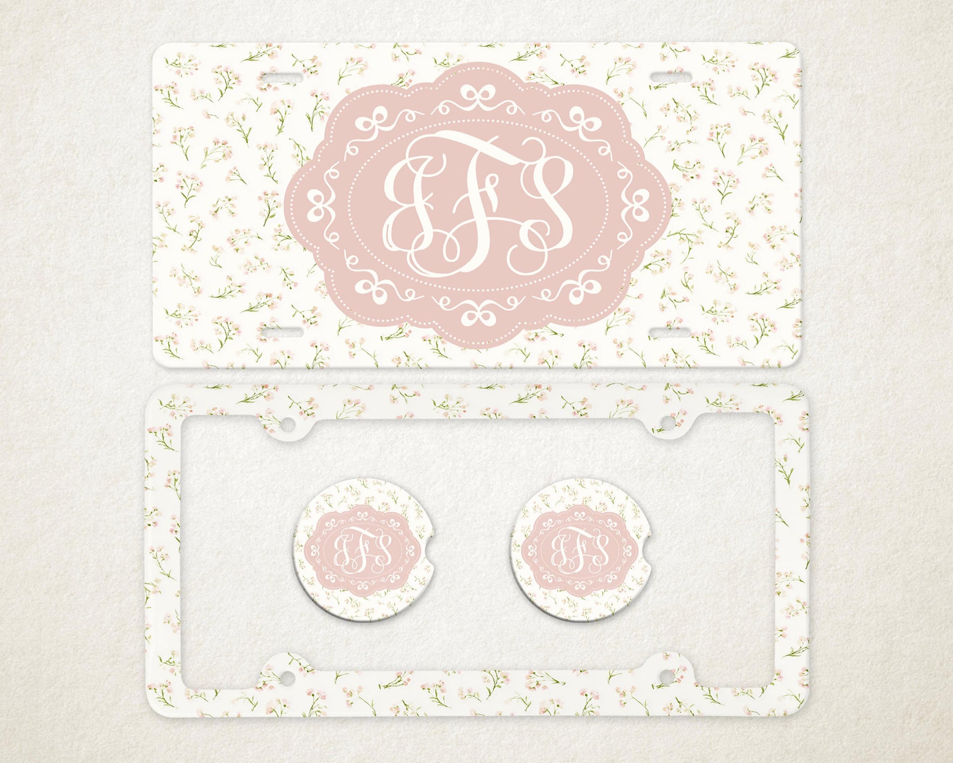 May include: A license plate, license plate frame, and two car coasters with a floral pattern. The license plate and coasters have a pink oval with the letters "JFS" in a white script. The license plate frame is clear.